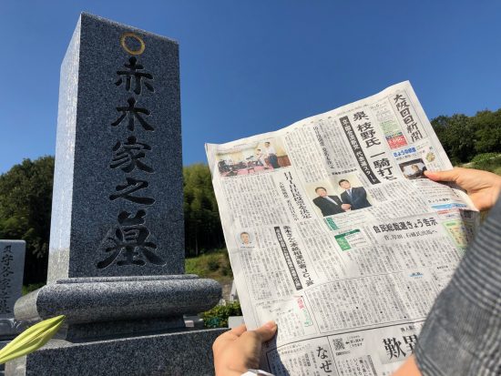 受賞決定を報じる新聞を掲げ墓前で報告する赤木雅子さん